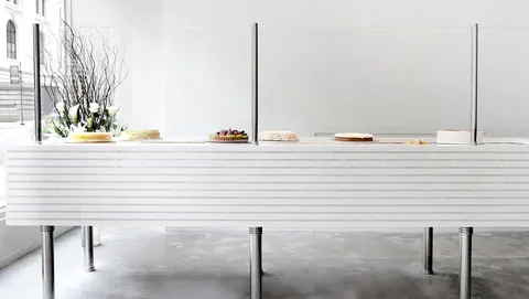 Bryant Park Lady M: minimalist cake display, white ribbed counter, chrome legs, cakes, white flowers. Bright.