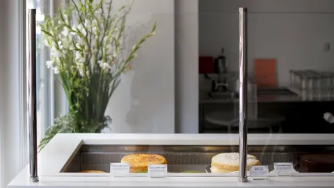 Lady M NoMad minimal cake display: whole cakes, description cards, elegant green and white floral arrangement.