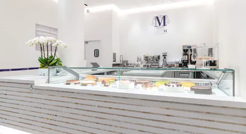 LADY M Arcadia interior with white display, glass pastry case, orchids, and logo on back wall.