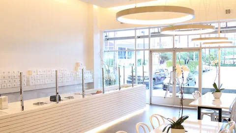 Lady M Irvine boutique with white counter, cake display, pendant lights, seating, and orchids.
