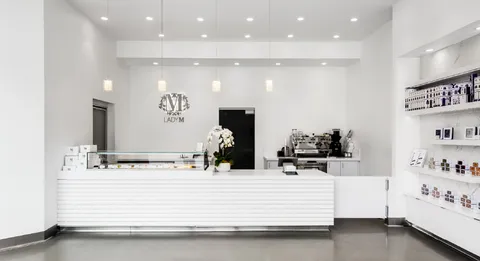 Lady M San Diego interior with white design, cake display, logo, pendant lights, and orchid.
