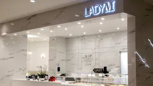 Elegant Lady M counter at Westfield Valley Fair: white marble, glowing logo, colorful cakes, white orchid, bright.