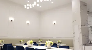 Bright, elegant dining area with white walls, sconces, navy chairs, flower-topped tables, and pendant lights.