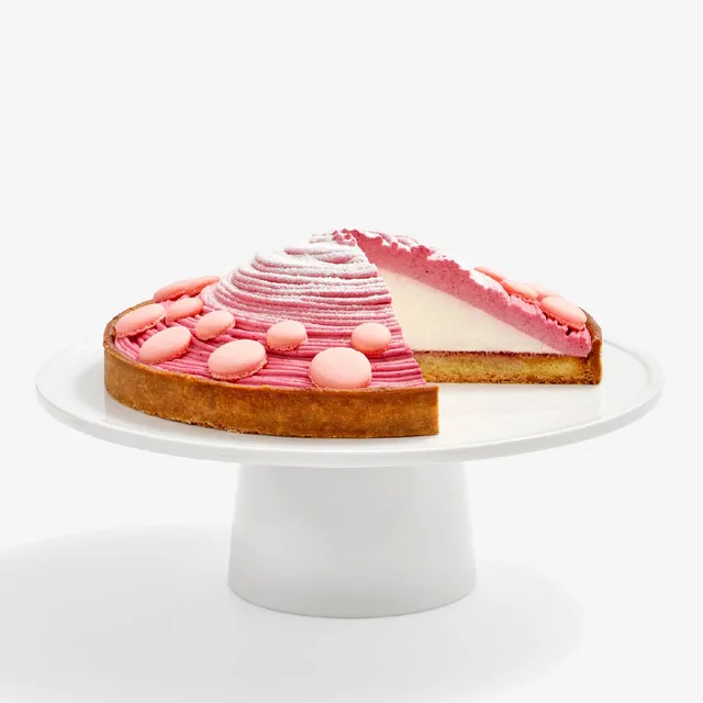 Berry Mont Blanc Tart sliced into revealing a center of fresh cream covered in four-berry mousse and topped with baby pink macaron shells and powdered sugar.