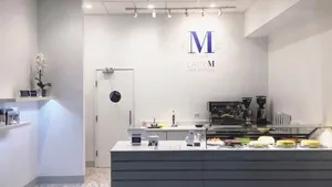 Modern white Lady M Chicago boutique with logo, gray counter, cake display, coffee machine, and white orchid.