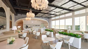Lady M Houston interior with chandeliers, natural light, white tables, and arched cake counter.