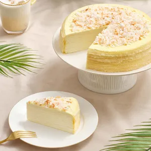 Lady M's Coconut Mille Crêpes with coconut flakes on white stand; slice and gold fork nearby.