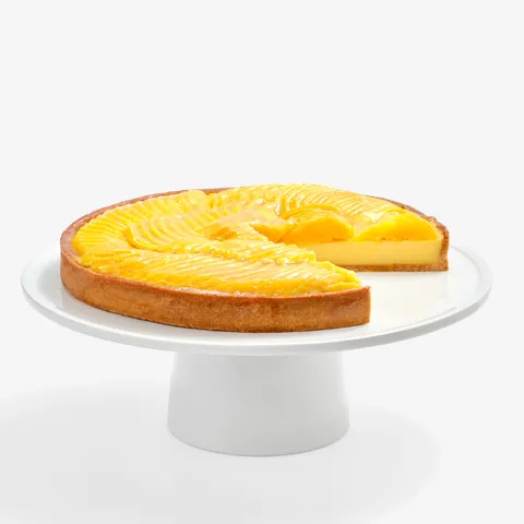 Lady M’s Tarte à la Mangue with passion fruit cream and glazed mango slices on a white cake stand.