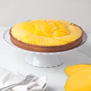 Lady M’s Tarte à la Mangue with a golden crust, passion fruit cream, mango slices, on a white stand.
