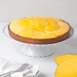 Lady M’s Tarte à la Mangue with a golden crust, passion fruit cream, mango slices, on a white stand.