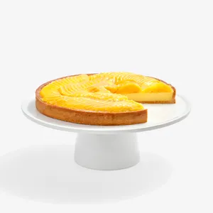 Lady M’s Tarte à la Mangue with passion fruit cream and glazed mango slices on a white cake stand.