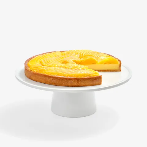 Lady M’s Tarte à la Mangue with passion fruit cream and glazed mango slices on a white cake stand.