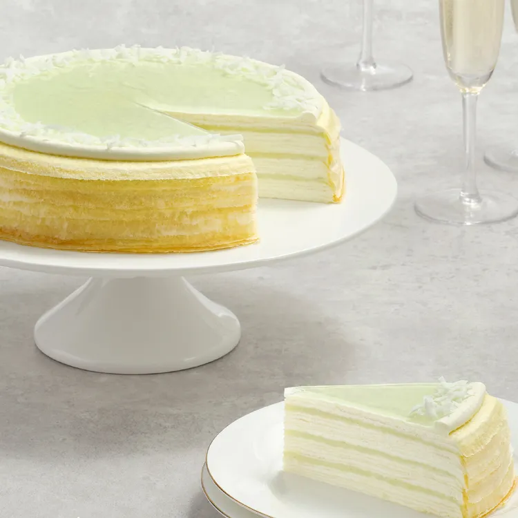Lady M Pandan Kaya Mille Crêpes with green glaze and slice on gold rimmed plate, with champagne glasses.