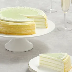 Lady M Pandan Kaya Mille Crêpes with green glaze and slice on gold rimmed plate, with champagne glasses.