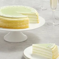 Lady M Pandan Kaya Mille Crêpes with green glaze and slice on gold rimmed plate, with champagne glasses.