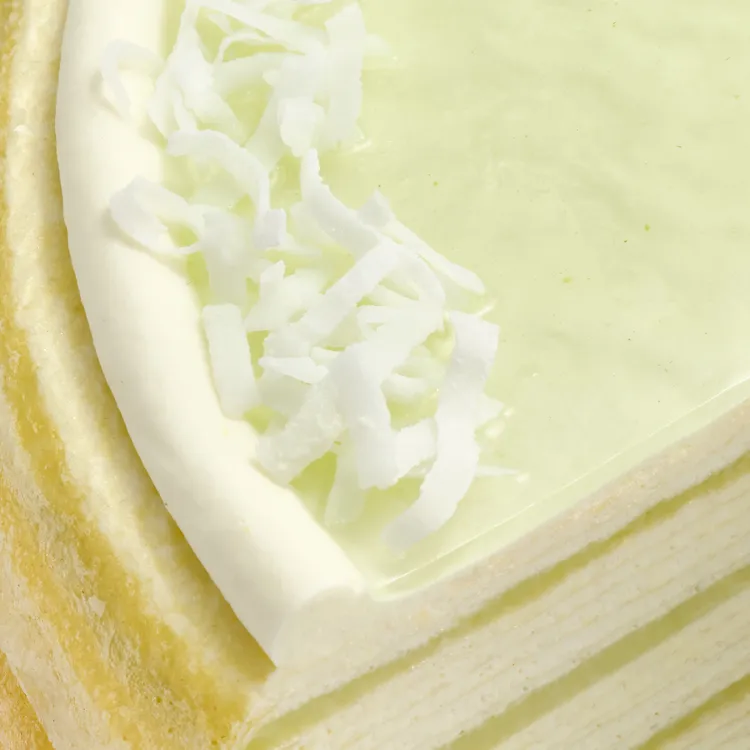 Close-up of Lady M Pandan Kaya slice with delicate crêpes, green glaze, cream, and coconut flakes.