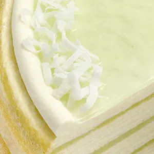 Close-up of Lady M Pandan Kaya slice with delicate crêpes, green glaze, cream, and coconut flakes.