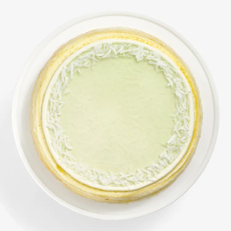 Overhead view of Lady M Pandan Kaya Mille Crêpes with green glaze, cream border, and coconut flakes.