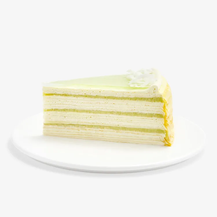 Slice of Lady M Pandan Kaya Mille Crêpes with cream, pandan custard, green glaze, and coconut.