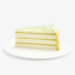 Slice of Lady M Pandan Kaya Mille Crêpes with cream, pandan custard, green glaze, and coconut.