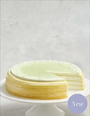 A Pandan Kaya Mille Crêpes cake on a white stand with a slice served on a plate.