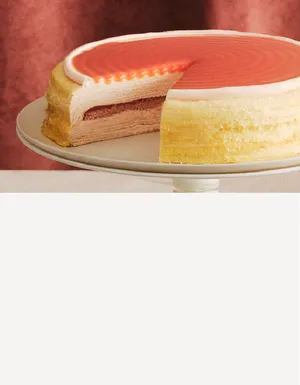 A Guava Mille Crêpes cake on a cake stand, with a slice cut and served on a plate.