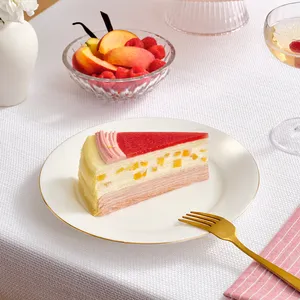 A slice of Peach Melba Mille Crêpes cake on a white plate with a gold fork next to it.