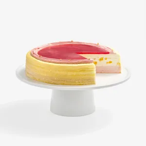 A Peach Melba Mille Crêpes cake on a white stand with one slice cut out to show the layers.