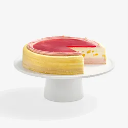 A Peach Melba Mille Crêpes cake on a white stand with one slice cut out to show the layers.