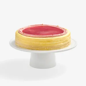 A whole Peach Melba Mille Crêpes cake with a red topping, presented on a white cake stand.