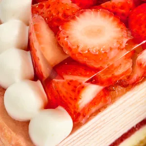 A macro close-up of sliced strawberries in gelée next to a border of white cream dollops.