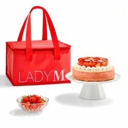 Lady M's Oishii Berry Trois cake on a stand, with a red tote bag and a bowl of fresh berries.