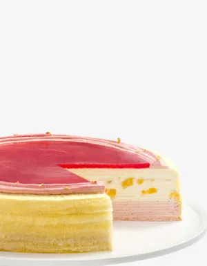 A Peach Melba Mille Crêpes cake on a glass stand with a slice cut out to show the layers.