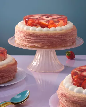 Lady M's Oishii Berry crêpe cake on a pink glass stand with a blue and iridescent background.
