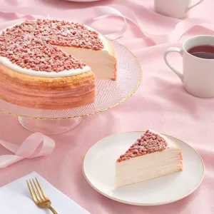 A Lady M Pink Pearl Mille Crêpes with one slice served on a plate, set on top a pink linen.