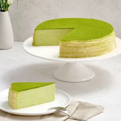A Lady M Gluten-Free Green Tea Mille Crêpes with one slice on a plate. Set on top a marble table.