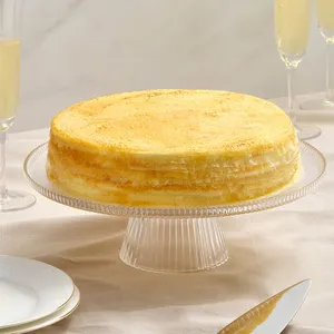 A Lady M Gluten-Free Signature Mille Crêpes on a glass cake stand, set over a linen table cloth.