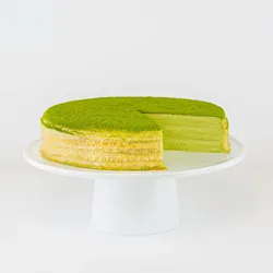 A sliced into Lady M Gluten-Free Green Tea Mille Crêpes on top a white cake stand.