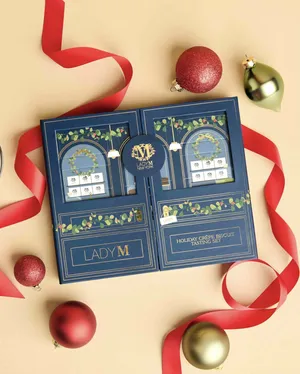 Lady M's Holiday Crêpe Biscuit Tasting Set on a beige surface with ribbon and ornaments.