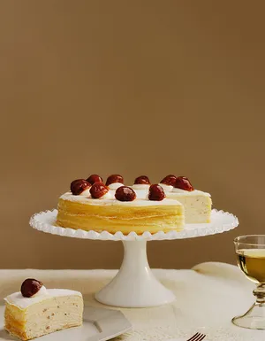 Lady M's Marron Mille Crêpes displayed on a table on a white scalloped cake stand.