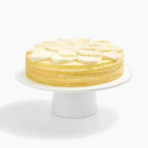 A whole Lady M Orange Mille Crepes cake on a white cake stand.