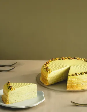 Lady M's Pistachio Mille Crêpes sliced into with a single slice on a beveled cake plate.