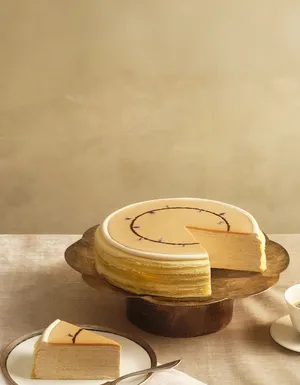 Lady M's Earl Grey Mille Crêpes on a metal cake stand and a beige tablecloth and backdrop.