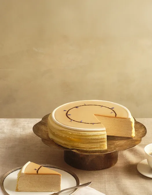Lady M's Earl Grey Mille Crêpes on a metal cake stand and a beige tablecloth and backdrop.