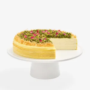 Baklava Mille Crêpes cake topped with pistachios, rose petals, and kataifi, with a slice removed.