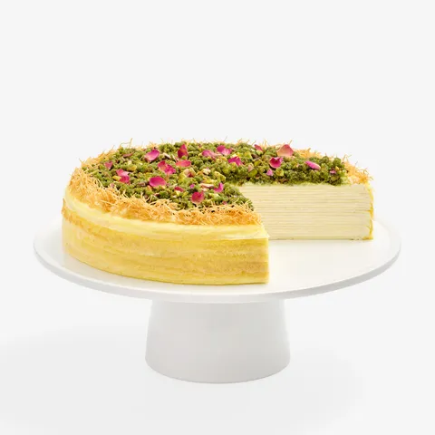 Baklava Mille Crêpes cake topped with pistachios, rose petals, and kataifi, with a slice removed.
