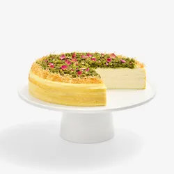Baklava Mille Crêpes cake topped with pistachios, rose petals, and kataifi, with a slice removed.