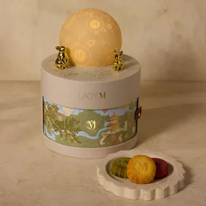 Lady M gift set with moon topper beside plate of three mooncakes