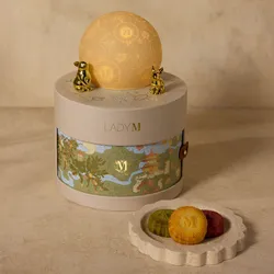 Lady M gift set with moon topper beside plate of three mooncakes