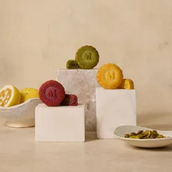 Three Lady M mooncakes on marble blocks with citrus and pistachios